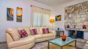 A living room with a beige sofa, a glass coffee table, a stone fireplace, and abstract wall art.