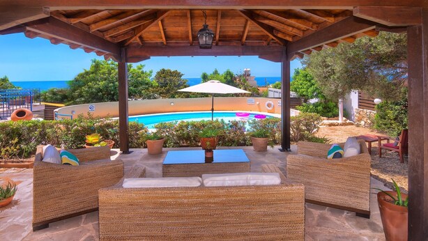 A covered outdoor seating area with wicker furniture, a pool, and a view of the sea.