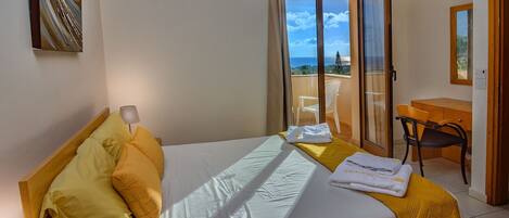 A hotel room with a bed, a desk, a chair, and a balcony with a view.