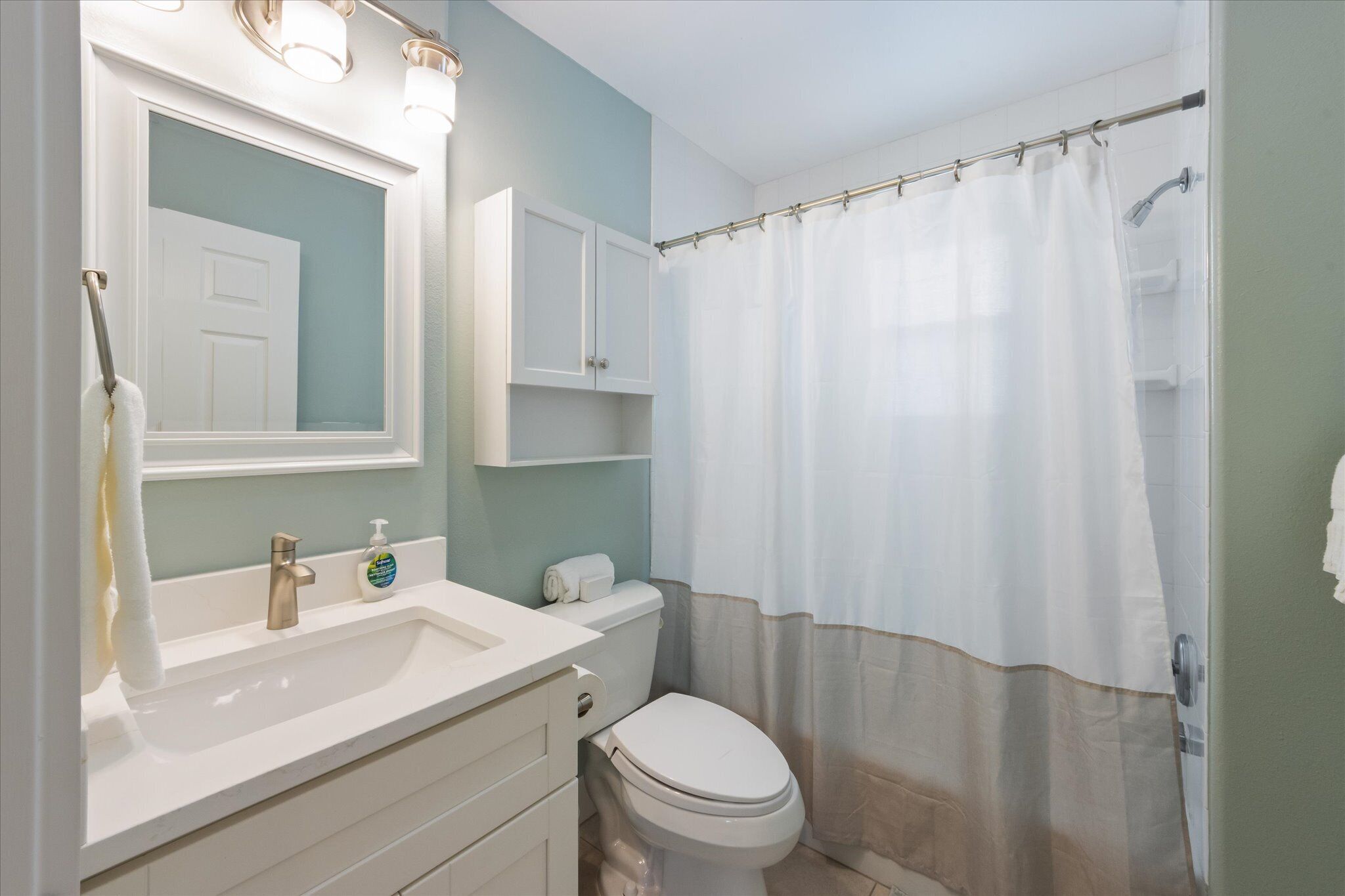 A bathroom with a sink, mirror, cabinet, toilet, and shower curtain.