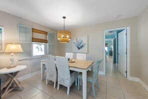 Uma área de refeições com mesa de madeira e cadeiras de vime, luminária pendente e um quadro na parede.