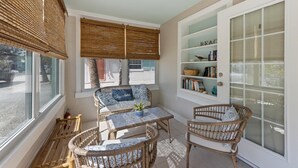 A sunlit room with wicker furniture, a glass door, and a shelf with decorative items. - Sea Spray 4: *Heated Pool *Pet-Friendly *Steps to beach *Shops, dining close (Anna Maria)