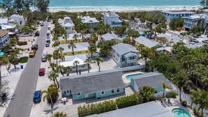 A coastal residential area with multiple houses, a swimming pool, and a beach in the background. - Sea Spray 4: *Heated Pool *Pet-Friendly *Steps to beach *Shops, dining close (Anna Maria)