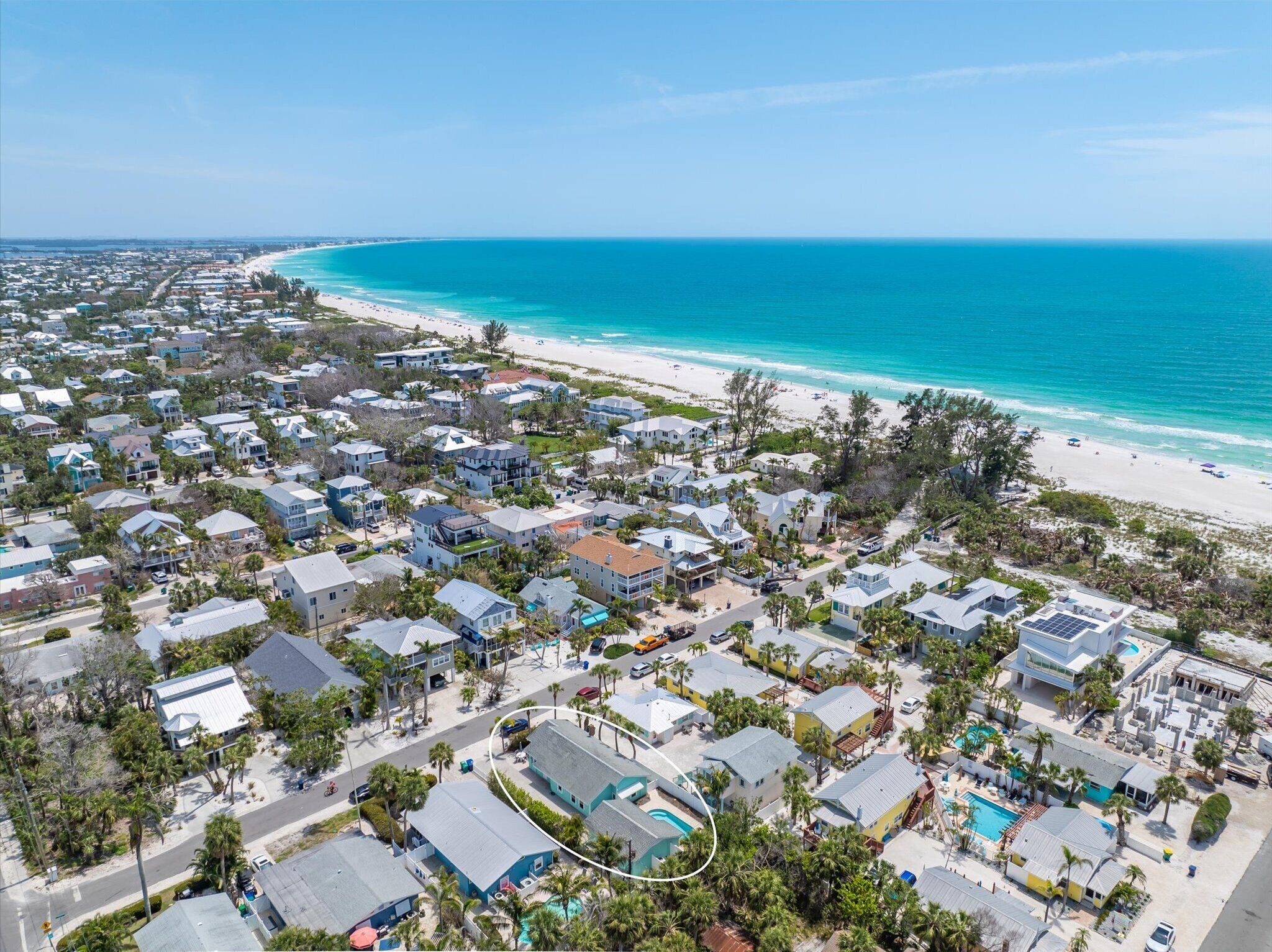 An aerial view of a coastal residential area with houses, a beach, and a clear blue sky.
