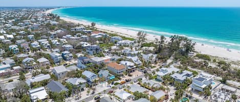 An aerial view of a coastal residential area with houses, a beach, and a clear blue sky.
