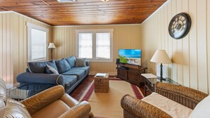 Un salon chaleureux avec un canapé bleu, un fauteuil en cuir marron, un canapé en osier, un téléviseur et une horloge au mur.