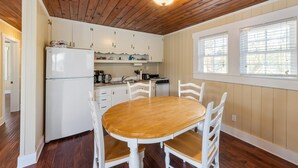 Une cuisine avec des meubles blancs, un réfrigérateur blanc et une table à manger en bois, assortie de chaises blanches.