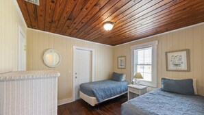 Une chambre avec deux lits, un plafond en bois, un miroir rond et une fenêtre avec des stores.