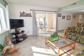 A living room with a television, a sofa, a coffee table, and a sliding glass door leading to a balcony.