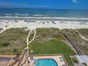 A beach resort with a swimming pool, beach umbrellas, and a boardwalk.