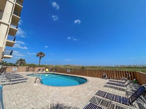 A swimming pool with lounge chairs, a palm tree, and a clear blue sky.