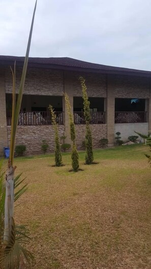A building with a stone facade, multiple windows, and a fenced yard with trimmed grass and a few trees.