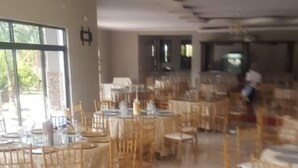 Un vaste espace dédié à la salle à manger, avec plusieurs tables rondes et des chaises en bois, de grandes fenêtres et un design moderne au niveau du plafond.