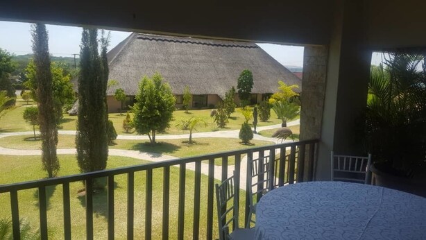 Un balcon offrant une vue sur un bâtiment à toiture de chaume, entouré de pelouses et d’arbres bien entretenus.