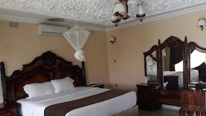 Une chambre à coucher avec un grand lit, une tête de lit en bois, un ventilateur de plafond, un miroir et une table de chevet.