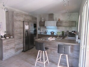 A modern kitchen with a built-in refrigerator, a dining area with two bar stools, and a large island with a sink.