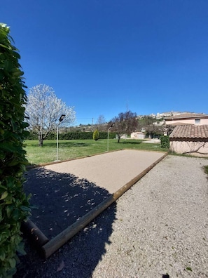 A clear outdoor area with a paved path, a small garden, and a building with a tiled roof in the background.