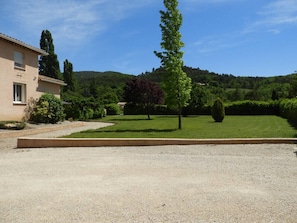 Um edifício com entrada por um caminho de cascalho, gramado bem cuidado e paisagem montanhosa ao fundo.