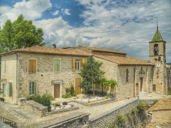 A stone building with a tiled roof, a bell tower, and a small courtyard with plants.