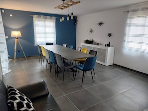 Uma sala de estar moderna com área de jantar, apresentando um sofá cinza, uma mesa de jantar com cadeiras azuis e amarelas e um abajur.