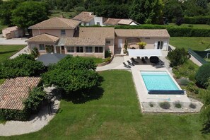 A large house with a swimming pool, surrounded by a well-maintained lawn and trees.