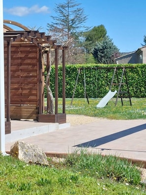 Uma estrutura de pérgola de madeira com balanço e escorrega em um quintal ajardinado.