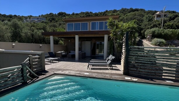 A swimming pool with clear water, a covered patio with lounge chairs, and a house in the background. - Villa Ghjulia (Porto-Vecchio)
