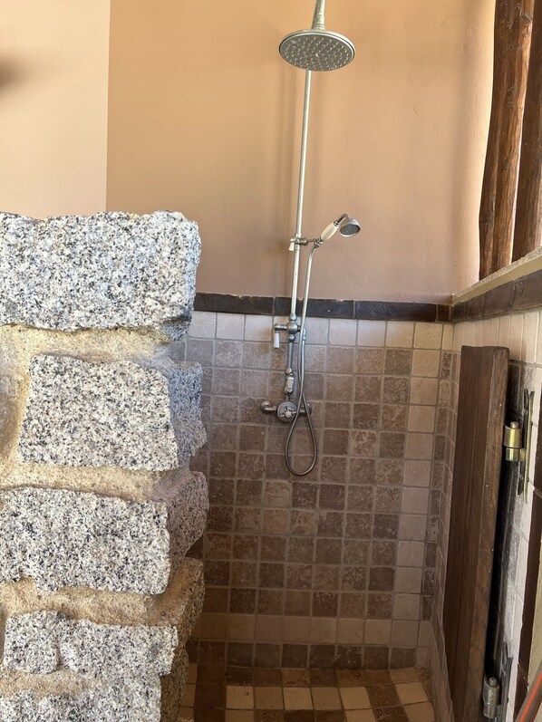 A shower area with a stone wall, tiled floor, and a wooden door.