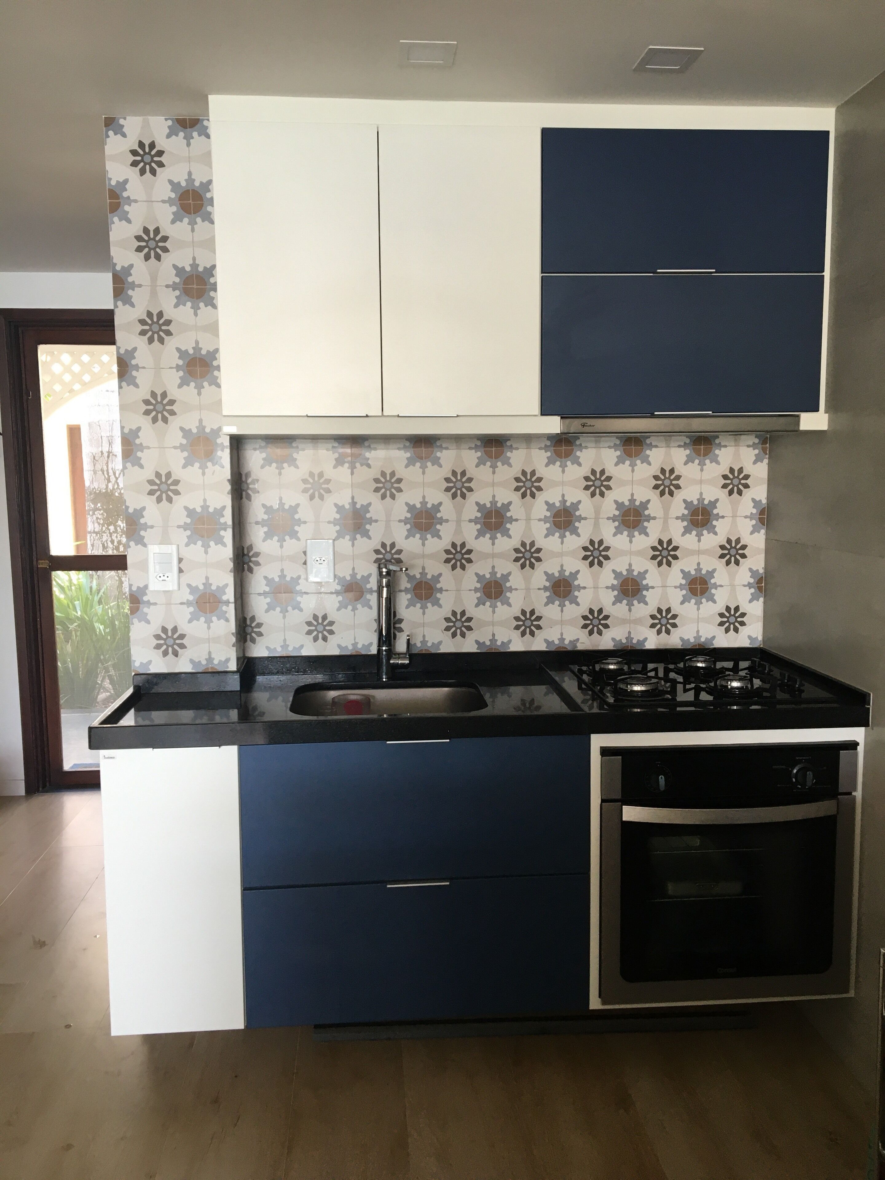 A kitchen with a gas stove, oven, and sink. There are cabinets above the counter and a patterned backsplash.
