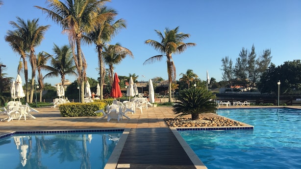 A swimming pool with a wooden deck, surrounded by palm trees and white lounge chairs.