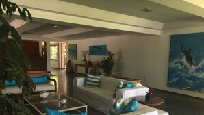 A modern living room with a white sofa, blue cushions, a glass coffee table, and a large abstract painting on the wall.