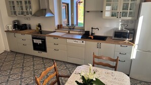 A kitchen with white cabinets, a wooden countertop, a Bosch dishwasher, a coffee maker, and a window with a view of a garden.