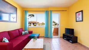 A living room with a red sofa, a wooden coffee table, a TV stand, and a view of a balcony with a railing. - Beautiful Apartment in Parque las Flores (Puerto de la Cruz)