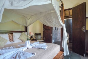 A bedroom with a four-poster bed, a sitting chair, and a statue. - Luxury Beach Villa with Infinity Pool. (Singaraja)