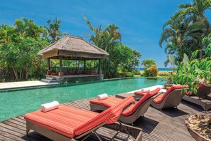 A poolside area with lounge chairs and a thatched-roof structure. - Luxury Beach Villa with Infinity Pool. (Singaraja)