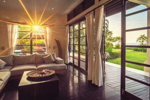 A spacious living room with a large window, a sofa, and a coffee table. - Luxury Beach Villa with Infinity Pool. (Singaraja)