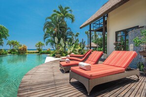 A wooden deck with lounge chairs and a pool, overlooking a beach and ocean.