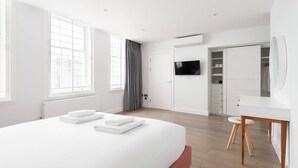 Ein modernes Schlafzimmer mit einem großen Bett, einem Fernseher, einem Kleiderschrank und einem Schreibtisch.