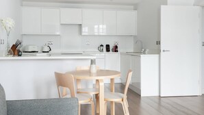 Eine moderne Küche mit weißen Schränken, einem Essbereich mit rundem Tisch und Stühlen sowie einem eingebauten Ofen.