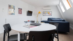 A modern living room with a round table, black chairs, a blue sofa, and artwork on the walls.