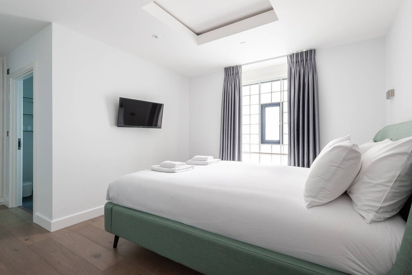 Une chambre d’hôtel moderne dotée d’un grand lit, d’un téléviseur à écran plat fixé au mur et d’une lucarne située au-dessus du lit.