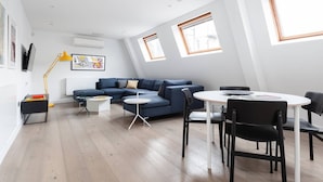 A modern living room with a blue sofa, a round dining table with chairs, a small coffee table, and a floor lamp.