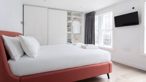 A modern hotel room with a large bed, a wardrobe, a television, and a window with curtains.