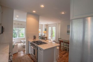 Kitchen with central island, stove, oven, and sink, connected to a dining area with a table and chairs.