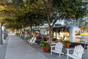 Relax in a casual outdoor dining area with Adirondack chairs and potted plants, near a food truck and communal entertainment space.