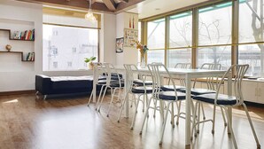 A modern dining area with a wooden floor, white chairs, and a table. - Cheese Guesthouse - Hostel (Seoul)