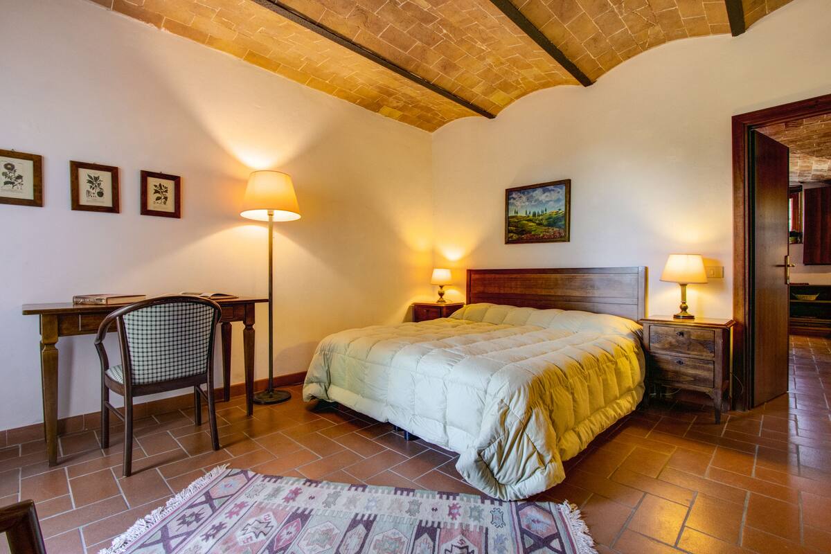 Une chambre à coucher avec un lit, deux tables de chevet avec des lampes, un bureau avec une chaise et un tapis.