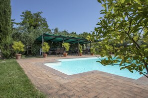 A swimming pool with a brick patio, surrounded by potted plants and a covered seating area. - Agriturismo Filettro (Volterra)
