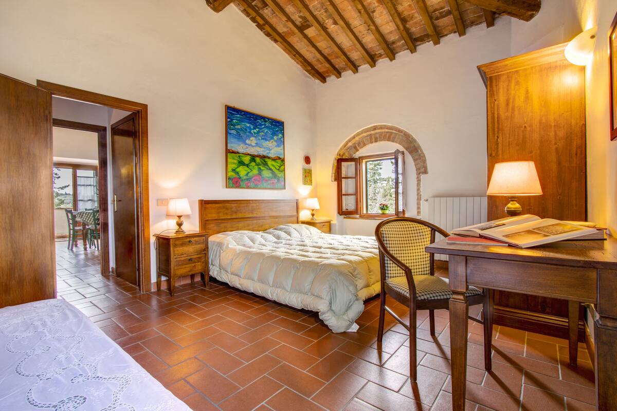 Une chambre à coucher avec un lit, un bureau avec une lampe, une chaise, un tableau et une fenêtre en arc de cercle.