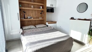 A bedroom with a bed, wooden shelving, a desk, a mirror, and a radiator. - Athens Studio in the sky...❗️❗️❗️ perfect for couples❤️️ (Kallithea)